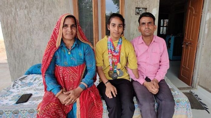 गोल्ड मेडल विजेता रनर तनीषा बाजिया अपने माता-पिता भंवरी देवी और इंद्राज बाजिया के साथ सीकर के अगलोई में अपने घर पर | फोटो: कृष्ण मुरारी/दिप्रिंट